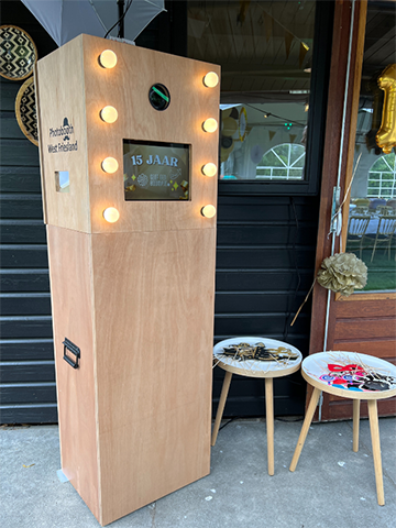 Compacte photobooth op statief met flitser in tropisch interieur.