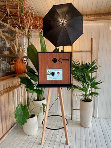Houten photobooth met lampjes en scherm bij feestlocatie.